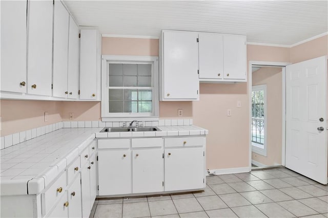 kitchen with sink, tile counters, light tile patterned flooring, white cabinets, and ornamental molding