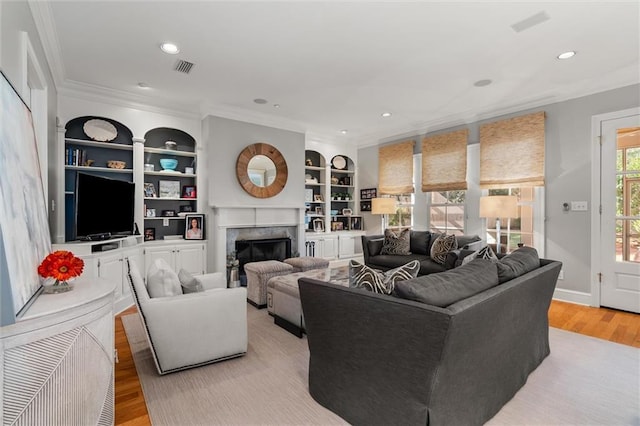 living room with built in shelves, light wood-type flooring, and ornamental molding