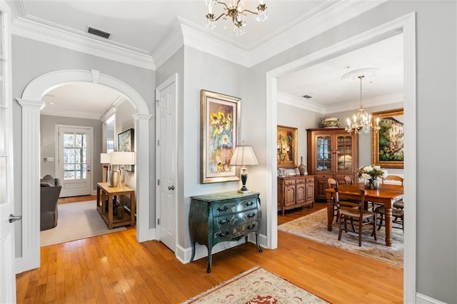 hallway with a chandelier, hardwood / wood-style floors, ornate columns, and crown molding