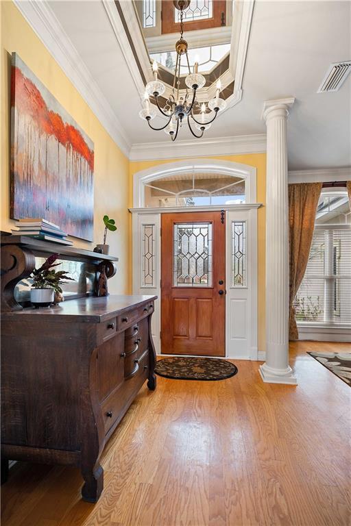 entryway featuring a chandelier, light wood-type flooring, decorative columns, and crown molding