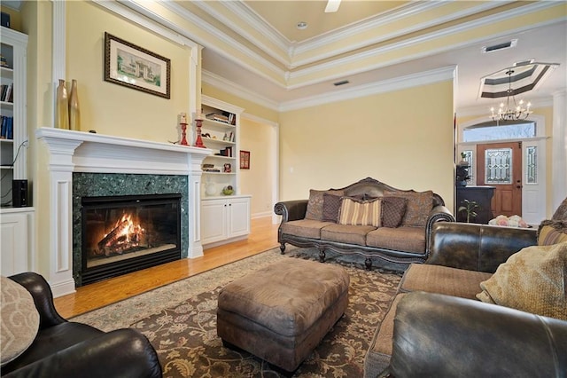 living room featuring a high end fireplace, built in features, ornamental molding, light hardwood / wood-style floors, and a chandelier