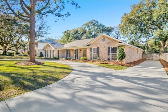 single story home with driveway, brick siding, fence, and a front yard