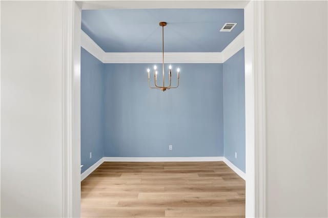 unfurnished dining area featuring ornamental molding, hardwood / wood-style floors, and a notable chandelier