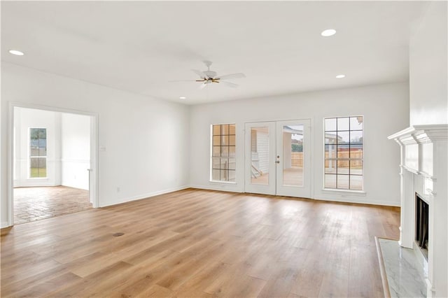 unfurnished living room featuring french doors, a fireplace, ceiling fan, and light hardwood / wood-style flooring