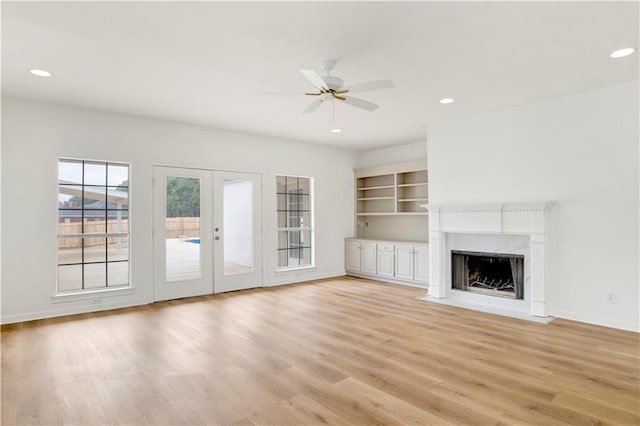 unfurnished living room featuring light hardwood / wood-style flooring, a premium fireplace, french doors, and ceiling fan