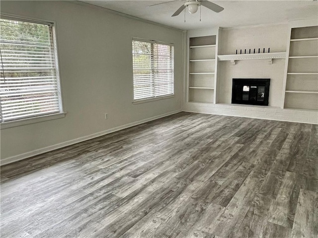 unfurnished living room featuring ceiling fan, built in shelves, and dark wood-type flooring