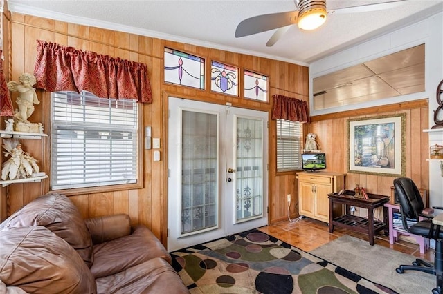 interior space featuring a ceiling fan, crown molding, wooden walls, and french doors