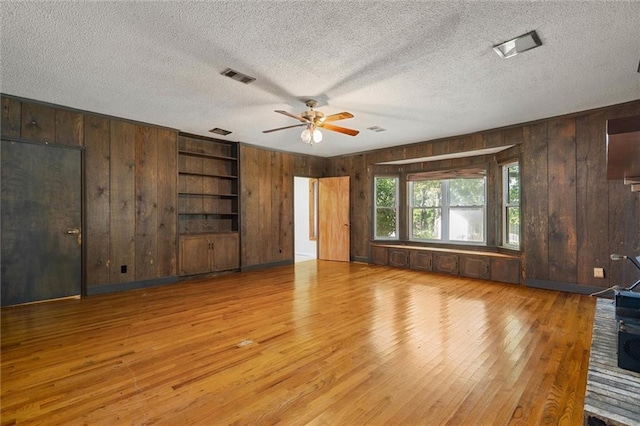 1113 4th Ave, Saraland, AL 36571 - unfurnished living room featuring wood walls, wood finished floors, ceiling fan, a textured ceiling, and built in shelves