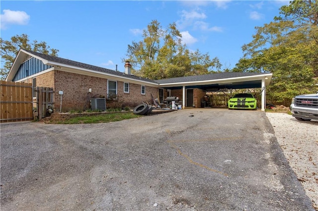 single story home featuring brick siding, central air condition unit, fence, an attached carport, and driveway