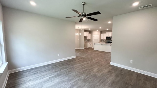 unfurnished living room with ceiling fan with notable chandelier and dark hardwood / wood-style flooring