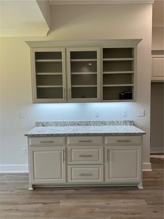 bar with light stone countertops, built in shelves, and wood-type flooring