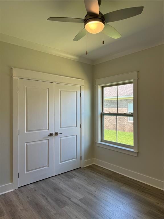 unfurnished bedroom featuring dark wood-type flooring, a closet, ceiling fan, and crown molding