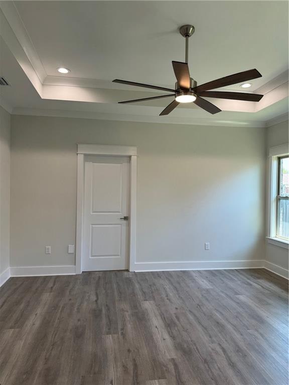 spare room featuring dark wood-type flooring, ornamental molding, ceiling fan, and a tray ceiling