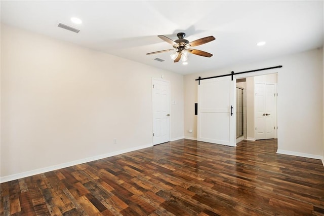 spare room featuring dark hardwood / wood-style floors, ceiling fan, and a barn door