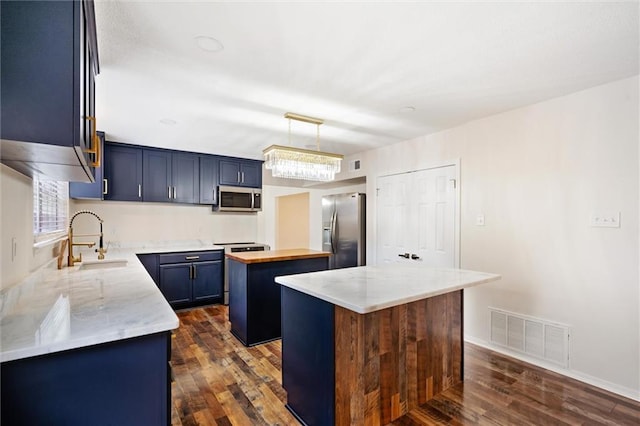 kitchen with blue cabinetry, sink, hanging light fixtures, appliances with stainless steel finishes, and a kitchen island