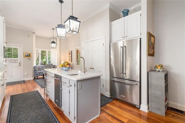 kitchen with high quality fridge, decorative light fixtures, light wood-type flooring, and an island with sink