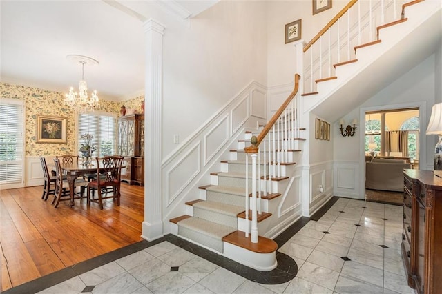 staircase with decorative columns, a chandelier, light wood-type flooring, and a healthy amount of sunlight