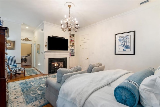 bedroom featuring washer / clothes dryer, ornamental molding, a notable chandelier, and hardwood / wood-style floors