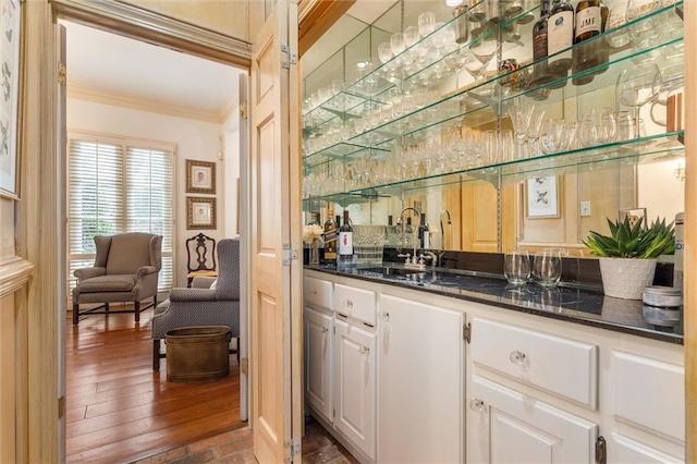 bar with dark stone counters, sink, crown molding, white cabinetry, and wood-type flooring