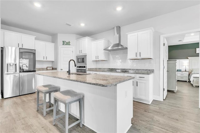 kitchen featuring appliances with stainless steel finishes, wall chimney range hood, a sink, white cabinetry, and a breakfast bar area