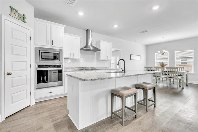 kitchen featuring stainless steel appliances, wall chimney exhaust hood, a sink, white cabinets, and light wood-type flooring