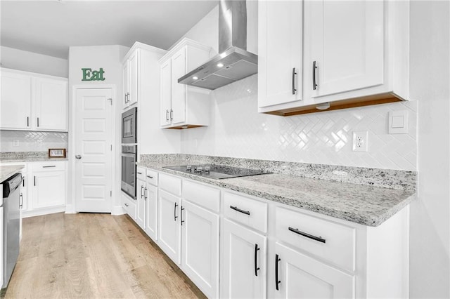 kitchen featuring wall chimney range hood, stainless steel appliances, light wood-style flooring, white cabinetry, and decorative backsplash