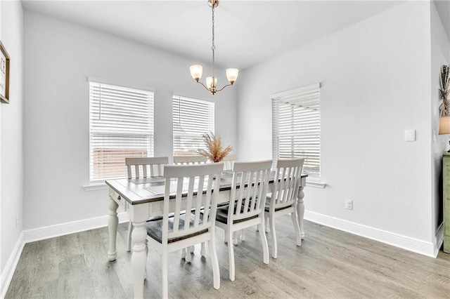 dining space with light wood-style flooring, a chandelier, and baseboards
