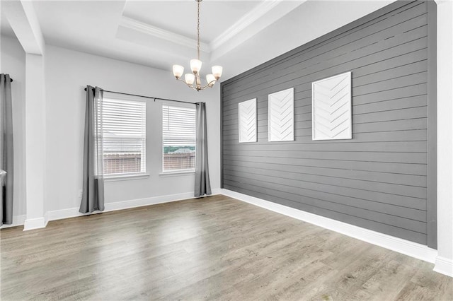 unfurnished dining area featuring a chandelier, wood finished floors, crown molding, a tray ceiling, and baseboards