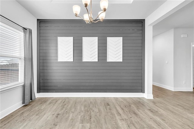 unfurnished dining area featuring a chandelier, baseboards, wood finished floors, healthy amount of natural light, and wood walls