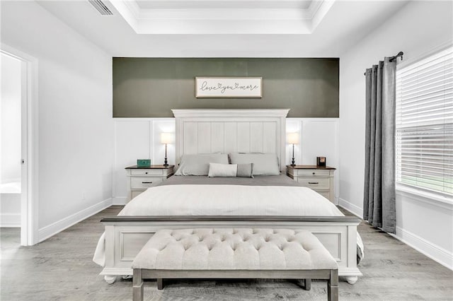 bedroom featuring light wood finished floors, a tray ceiling, crown molding, and baseboards