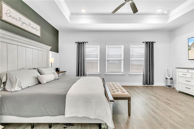 bedroom with a raised ceiling, light wood-style floors, crown molding, baseboards, and ceiling fan