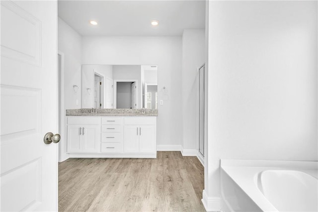 bathroom featuring a garden tub, double vanity, wood finished floors, and a shower with shower door