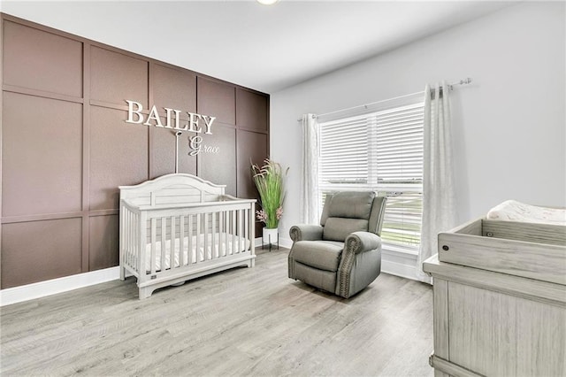 bedroom with baseboards, light wood-style floors, and a nursery area
