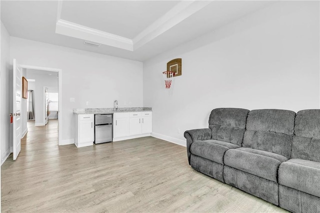 living area featuring a raised ceiling, light wood-type flooring, baseboards, wet bar, and ornamental molding