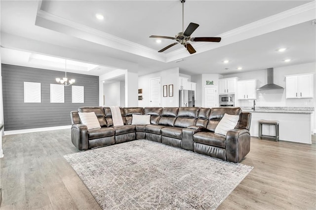 living room featuring a tray ceiling, a chandelier, ceiling fan, light wood finished floors, and recessed lighting