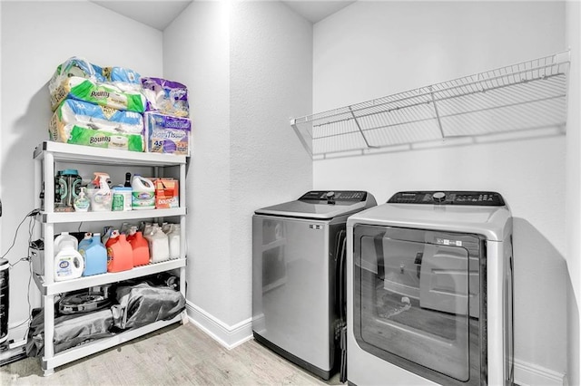 clothes washing area with washer and dryer, wood finished floors, and baseboards