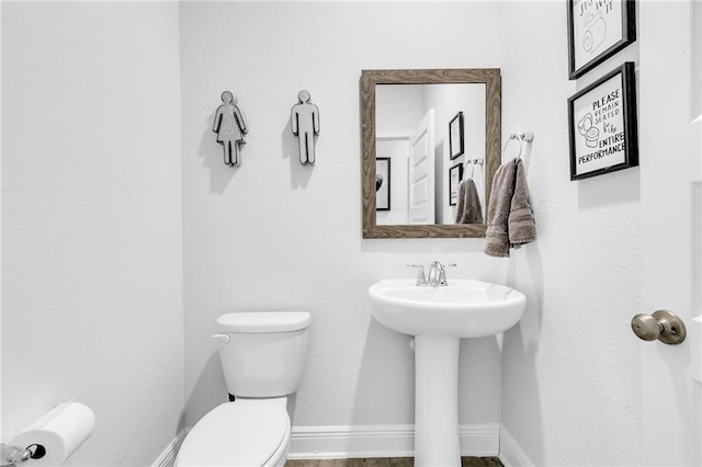 half bath featuring toilet, baseboards, and a sink
