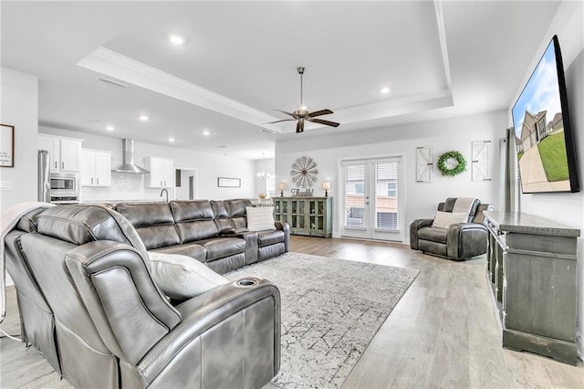 living room with a tray ceiling, a ceiling fan, light wood finished floors, crown molding, and recessed lighting