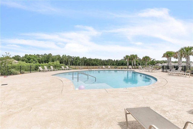 community pool with fence, a patio area, and view of wooded area