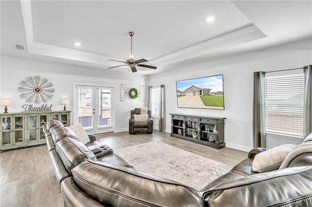 living room with a raised ceiling, crown molding, a ceiling fan, baseboards, and light wood finished floors