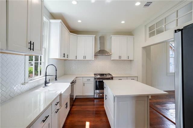 kitchen featuring wall chimney range hood, sink, stainless steel appliances, white cabinets, and dark hardwood / wood-style flooring