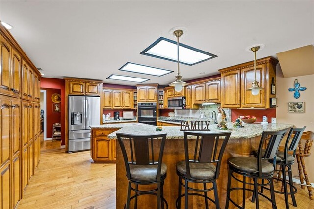 kitchen with pendant lighting, appliances with stainless steel finishes, light hardwood / wood-style floors, kitchen peninsula, and a skylight