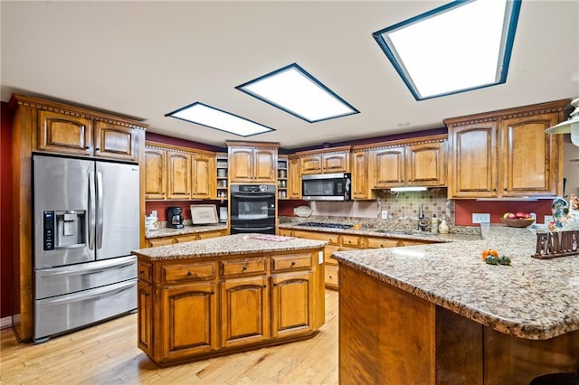 kitchen with light wood-type flooring, light stone countertops, stainless steel appliances, sink, and a kitchen island