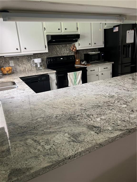 2618 Diberville Dr N, Mobile, AL 36695 - kitchen with black appliances, under cabinet range hood, light stone countertops, white cabinets, and decorative backsplash
