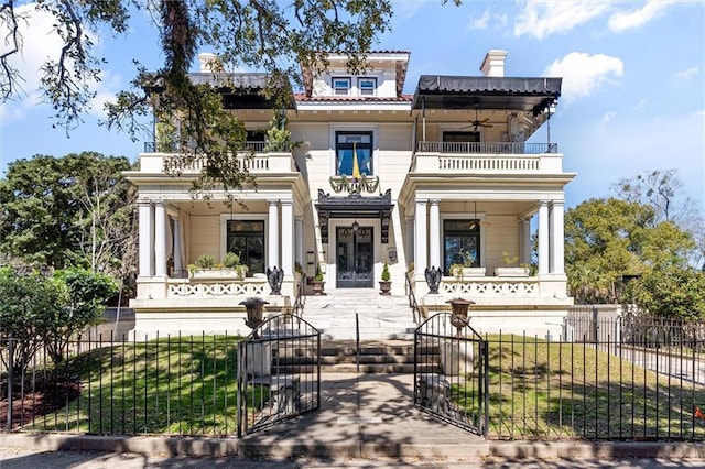 view of front of home with a fenced front yard, a balcony, a ceiling fan, and a gate