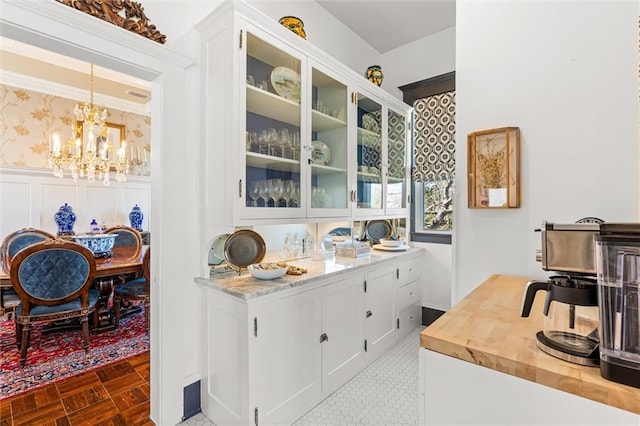 kitchen featuring wood counters, glass insert cabinets, wainscoting, and wallpapered walls