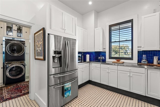 kitchen with stainless steel countertops, white cabinets, stainless steel refrigerator with ice dispenser, stacked washer and clothes dryer, and backsplash