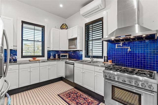 kitchen featuring a sink, a wall mounted air conditioner, appliances with stainless steel finishes, white cabinetry, and wall chimney range hood