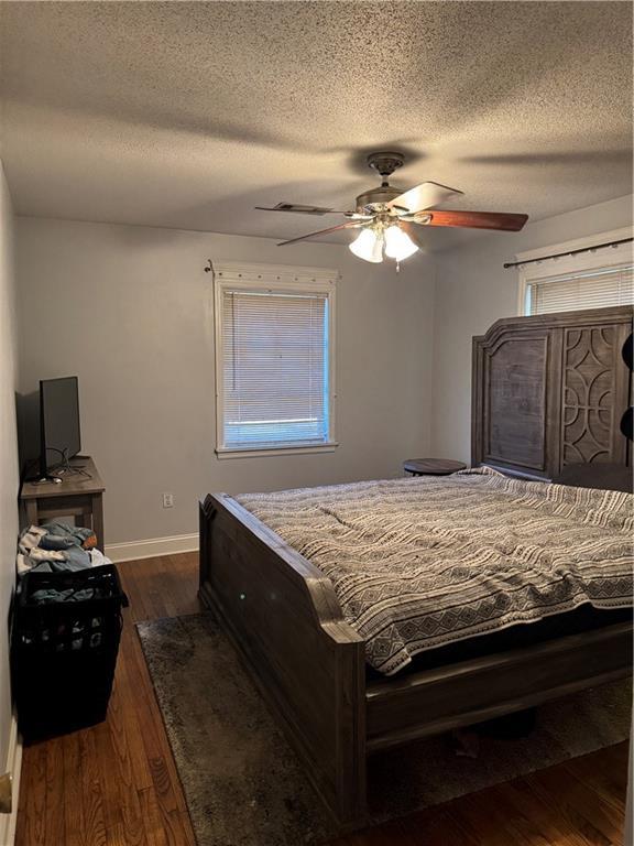 bedroom with ceiling fan, dark wood-type flooring, and a textured ceiling