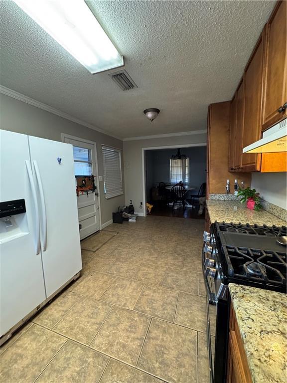 kitchen with gas range, a textured ceiling, white refrigerator with ice dispenser, and ornamental molding